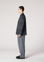 A person with short dark hair stands in profile against a plain background, wearing the IM MEN CURVINESS SHIRT, a dark patterned jacket, wide gray pants, and black shoes—evoking ceramic artist Shoji Kamoda's refined style.