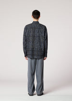 A person faces away from the camera, wearing the IM MEN CURVINESS SHIRT with a textured stripe and loose gray pants, echoing Shoji Kamoda’s minimalist style, set against a plain light background.