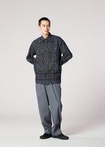 A person stands against a plain background, wearing the IM MEN CURVINESS SHIRT with textured stripes, loose gray trousers, and black shoes, hands in pockets, looking slightly to the side.