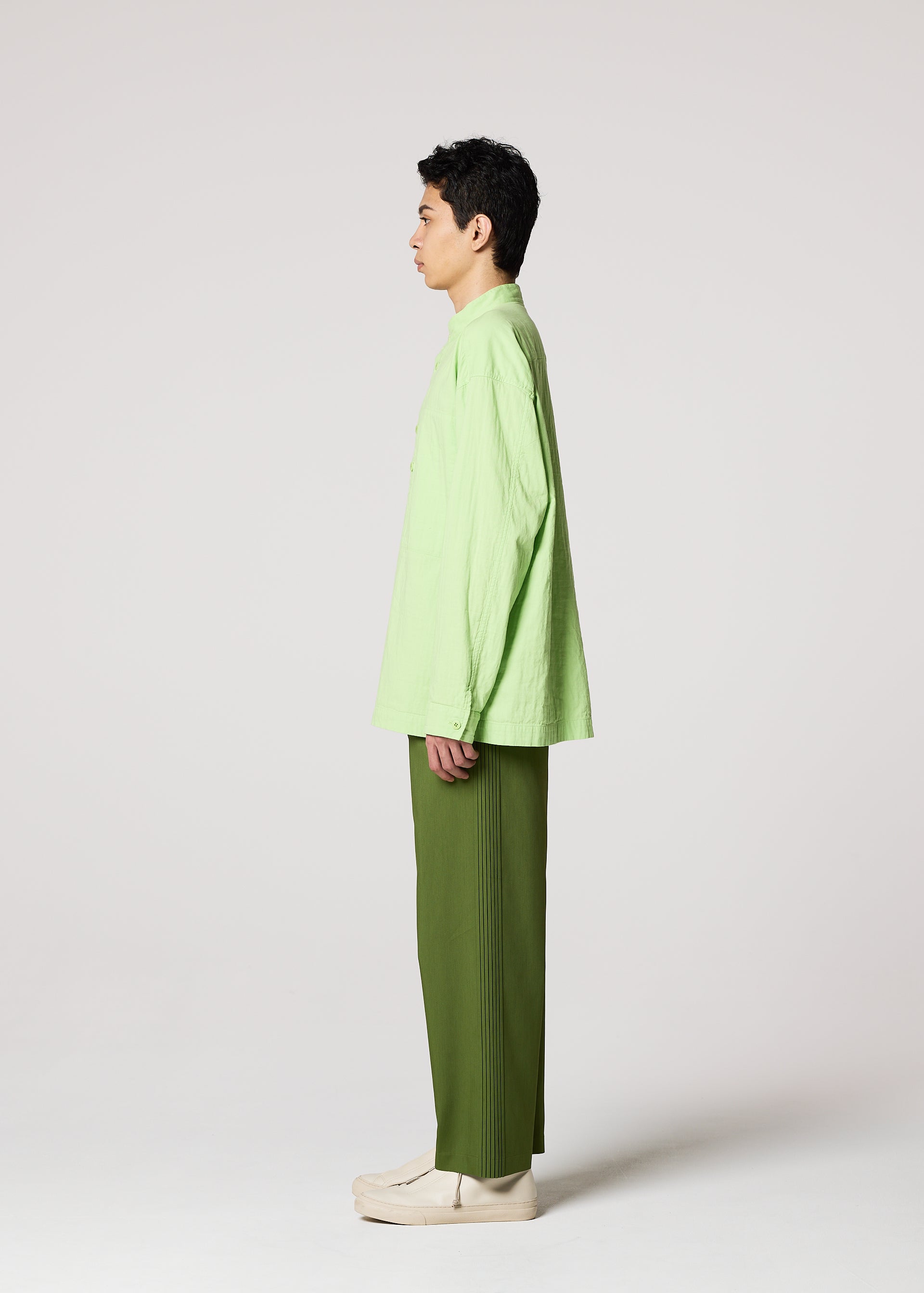 Zoomed view A person stands in profile against a plain background, wearing the IM MEN DOUBLE FACE COTTON SHIRT in light green, olive green pants, and cream-colored shoes.