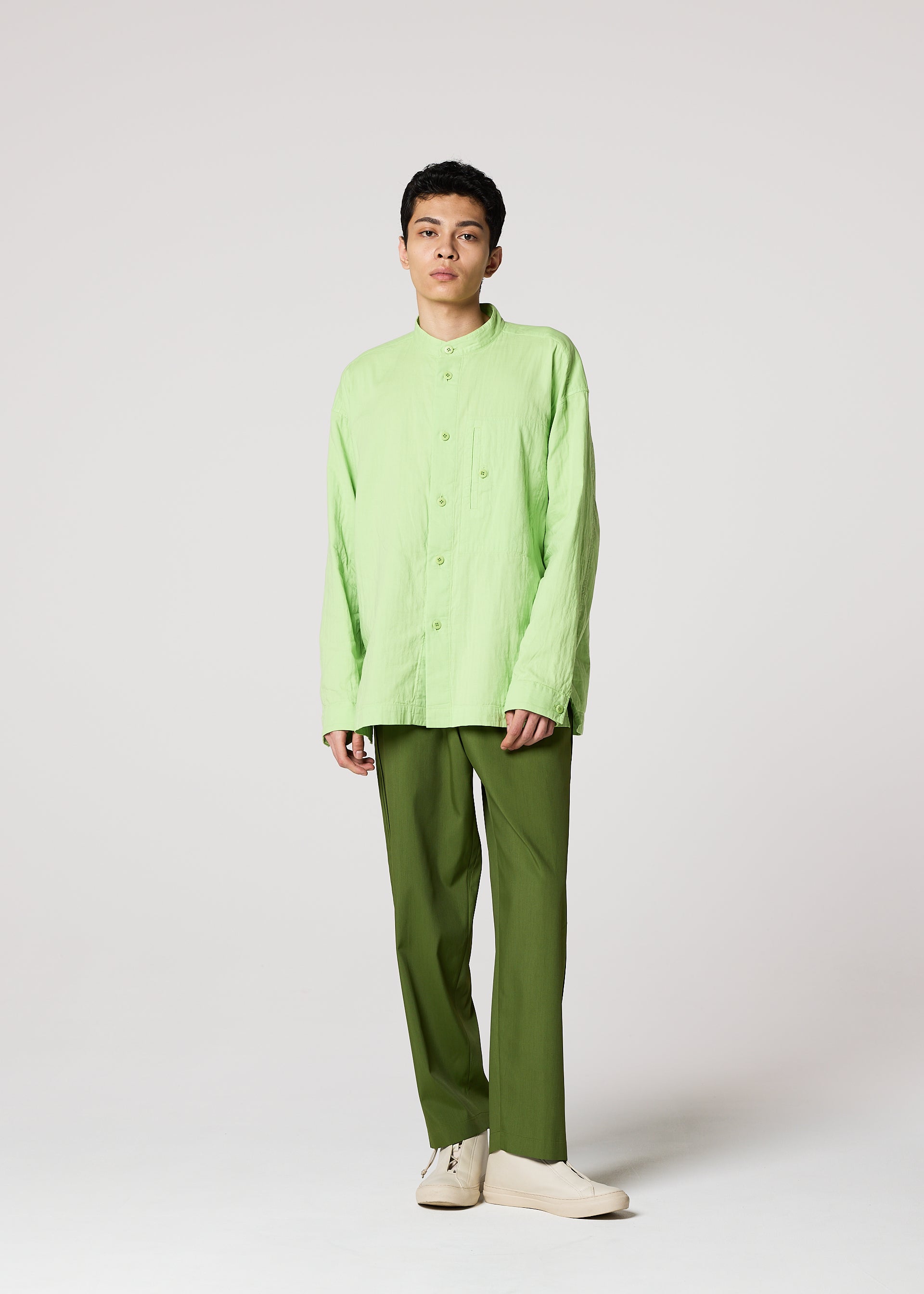 Zoomed view A person with short dark hair and a neutral expression wears the IM MEN DOUBLE FACE COTTON SHIRT—a loose, light green, double-woven cotton button-up—paired with olive pants and cream shoes, standing against a plain light background.