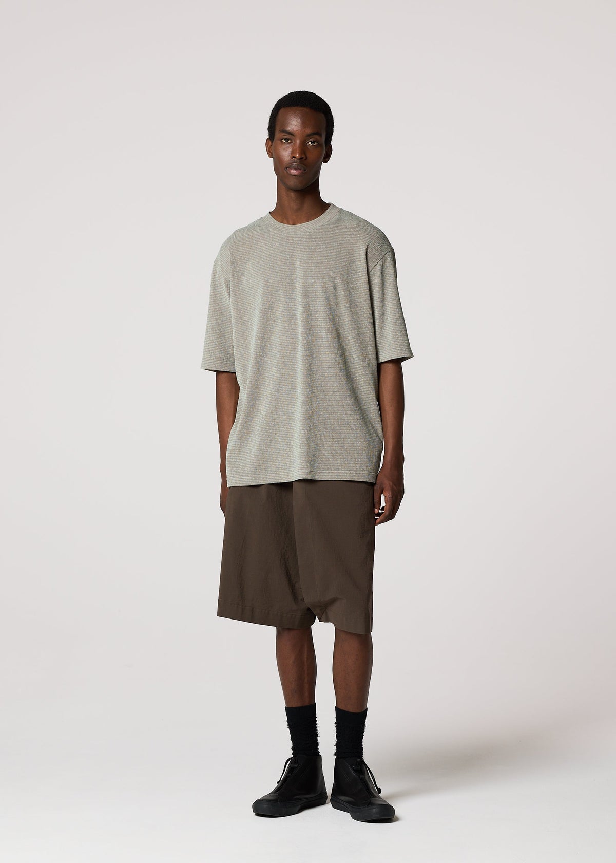 A man stands against a plain light background wearing the IM MEN SHRINK STRETCH T in gray, brown knee-length shorts, black socks, and black shoes. He faces forward with a neutral expression and relaxed posture. view 8 of 8