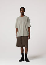 A man stands against a plain light background wearing the IM MEN SHRINK STRETCH T in gray, brown knee-length shorts, black socks, and black shoes. He faces forward with a neutral expression and relaxed posture.