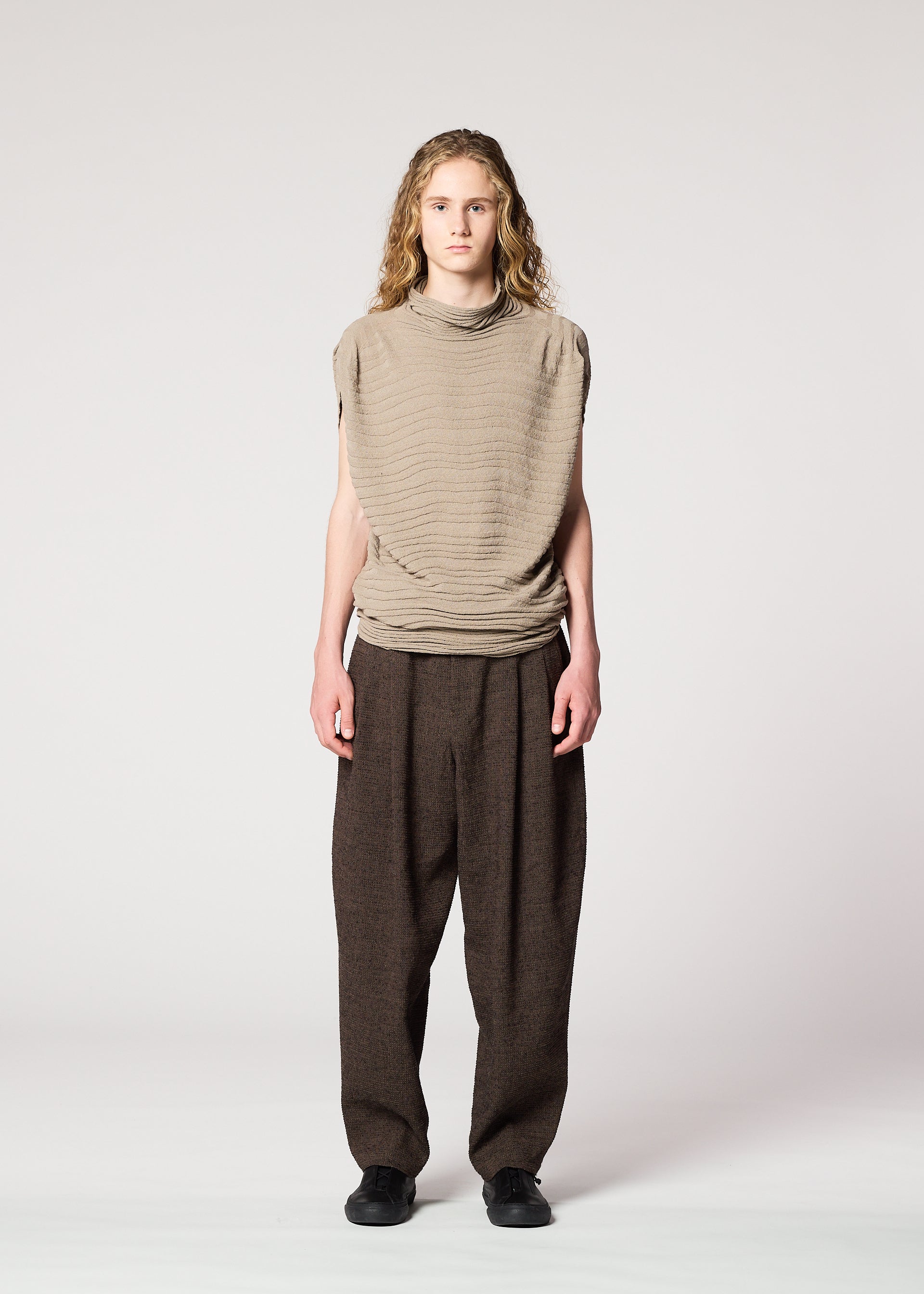 Zoomed view A person with long, wavy hair faces forward, wearing the IM MEN ENGRAVE KNIT top in beige and wide brown pants with black shoes against a plain light background.