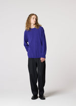 Against a plain background, a person with long curly hair wears the IM MEN COMFORT breathable, long-sleeved knit purple sweater, paired with black pants and shoes. They stand relaxed, looking slightly to the side.