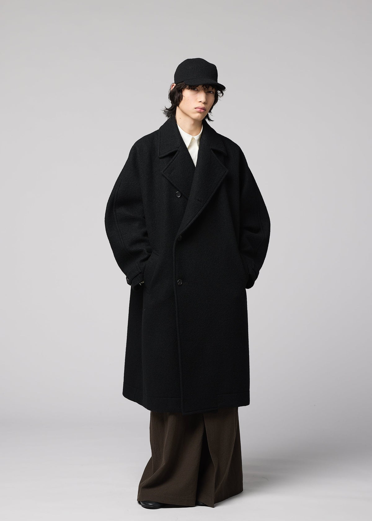 Zoomed view A person in a black overcoat, white shirt, wide brown pants, and the IM MEN FULLER WOOL CAP stands against a plain light gray background.