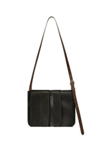 The LEATHER PLEATS shoulder bag by IM MEN, showcased against a white background, is crafted from natural black leather with elegant pleats, featuring three vertical front panels and a long, adjustable brown strap. This piece is part of the IM MEN Autumn Winter 2026/27 Collection. - BLACK （no.15）