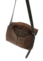The LEATHER PLEATS crossbody bag by IM MEN features brown natural leather, a long adjustable strap, an open top, visible inner zippered pocket, and snap closures. Part of the IM MEN Autumn Winter 2026/27 Collection, this empty shoulder bag is photographed against a white background.