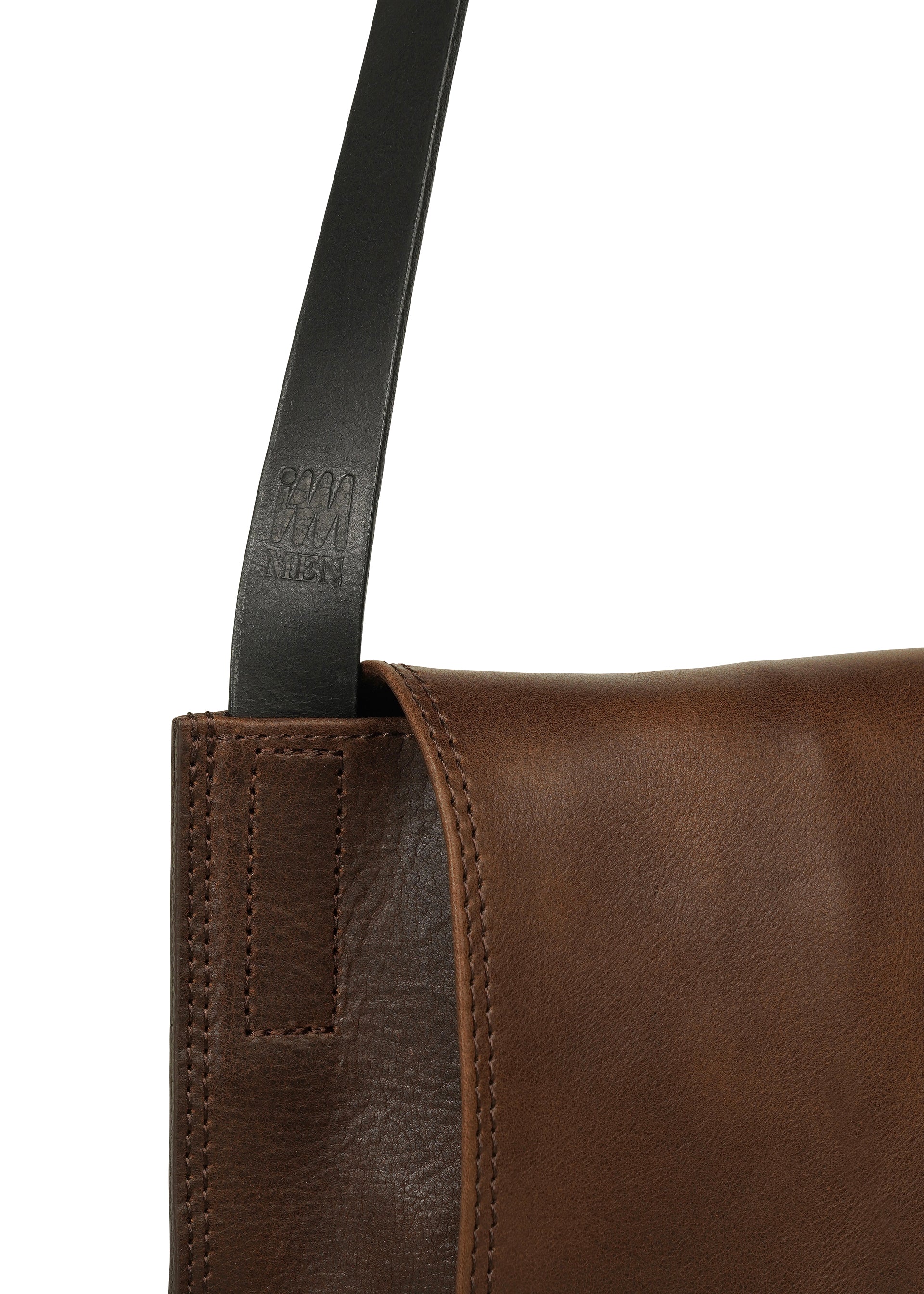Zoomed view Close-up of the LEATHER PLEATS shoulder bag by IM MEN, crafted from brown natural leather with visible stitching and a black strap. The strap, part of the IM MEN Autumn Winter 2026/27 Collection, features embossed text near the edge of the bag.