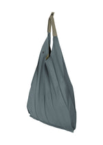 The IM MEN GURU GURU is a blue-gray foldable tote bag with handmade pleats, chic S-shaped curves, and a beige handle, shown against a white background.