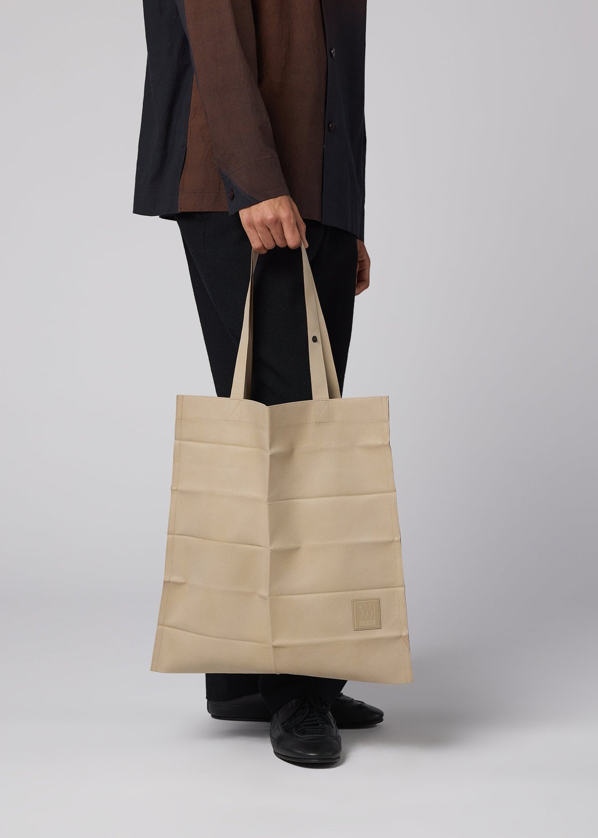 Zoomed view A person in black pants and a dark shirt holds an IM MEN PATA PA foldable tote bag with horizontal stripes and two handles, standing against a plain light background.