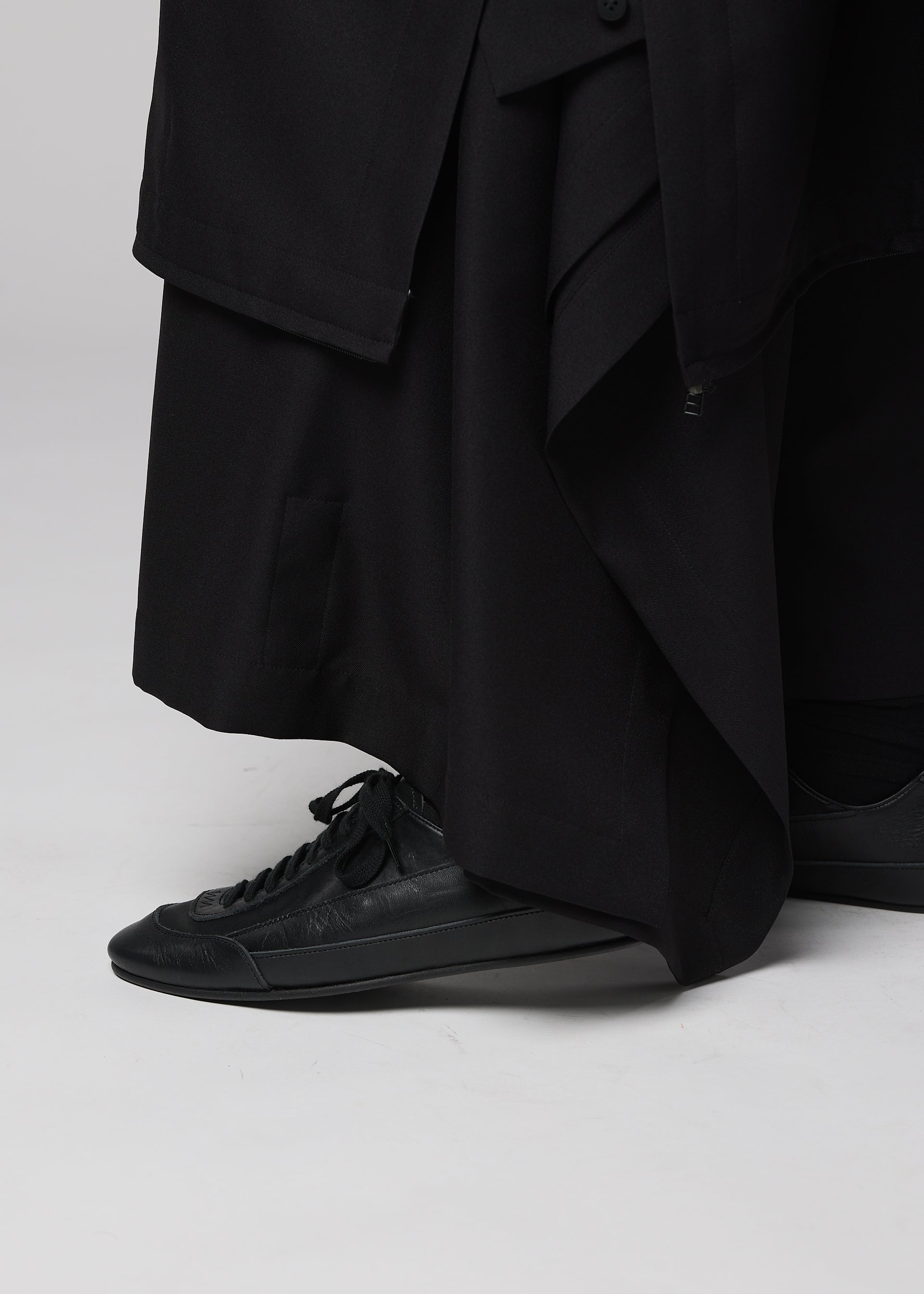 Zoomed view A person wearing the IM MEN FLIPPER long black garment and black lace-up sneakers featuring a cushioned insole stands on a light gray surface.