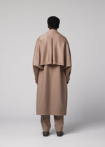 A person stands facing away, dressed in the FRONT BACK long taupe wool coat with matching over-cape and pants by IM MEN, from the Autumn Winter Collection, set against a plain light gray background.