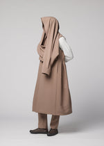 A person stands against a light background wearing the FRONT BACK beige wool coat by IM MEN, with fabric draped over their head to conceal their face and upper body. Their hands are behind their back.