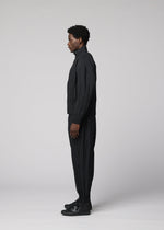 A person stands in profile facing left, dressed in IM MEN’s WAFT BLACK polyester jacket with a subtle linen-like texture, black pants, and black shoes against a plain light gray background.