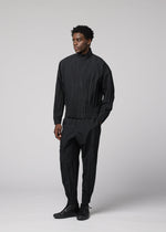 A person stands against a light gray background, wearing the IM MEN WAFT BLACK set: a loose-fitting polyester jacket and matching pleated black pants with a linen-like texture, paired with black shoes. They look slightly to the side with a neutral expression.