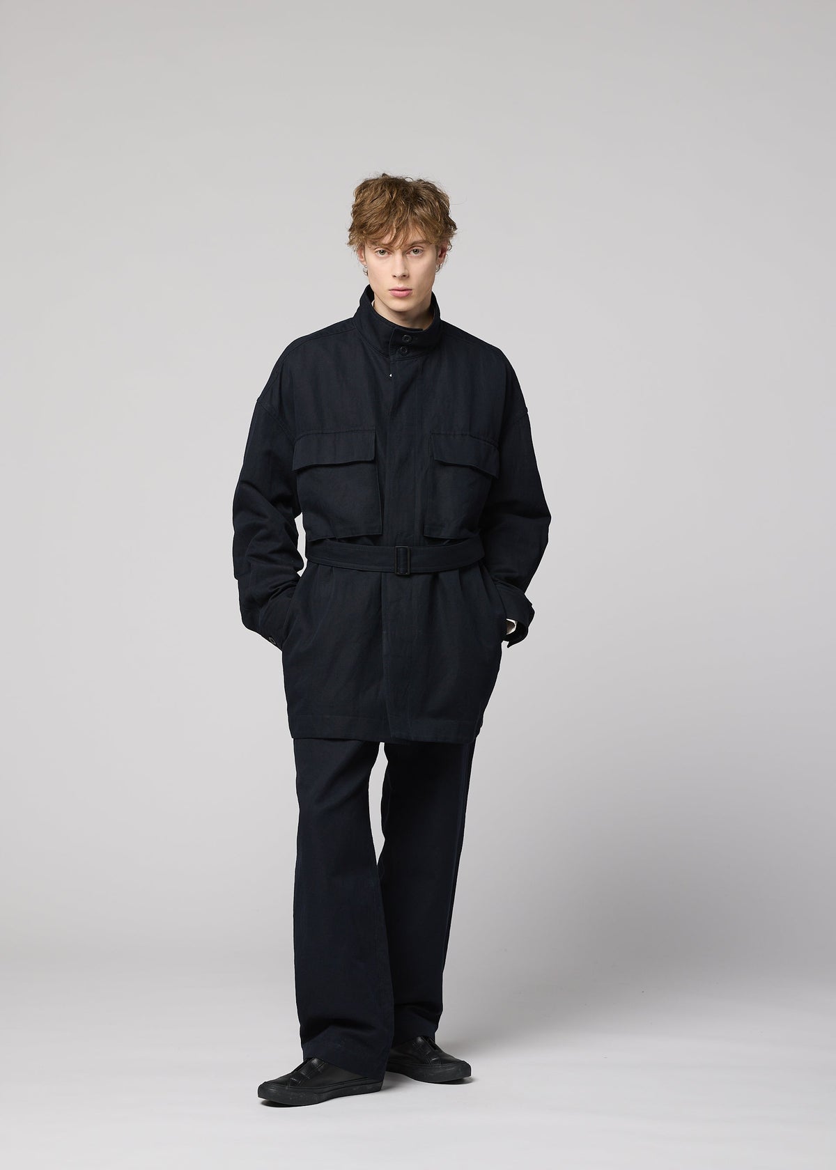 A person with tousled hair stands against a plain background wearing the IM MEN TOUGH WOOL COTTON belted jacket, wide-leg pants, and black shoes, looking toward the camera with their hands in their pockets. view 9 of 9