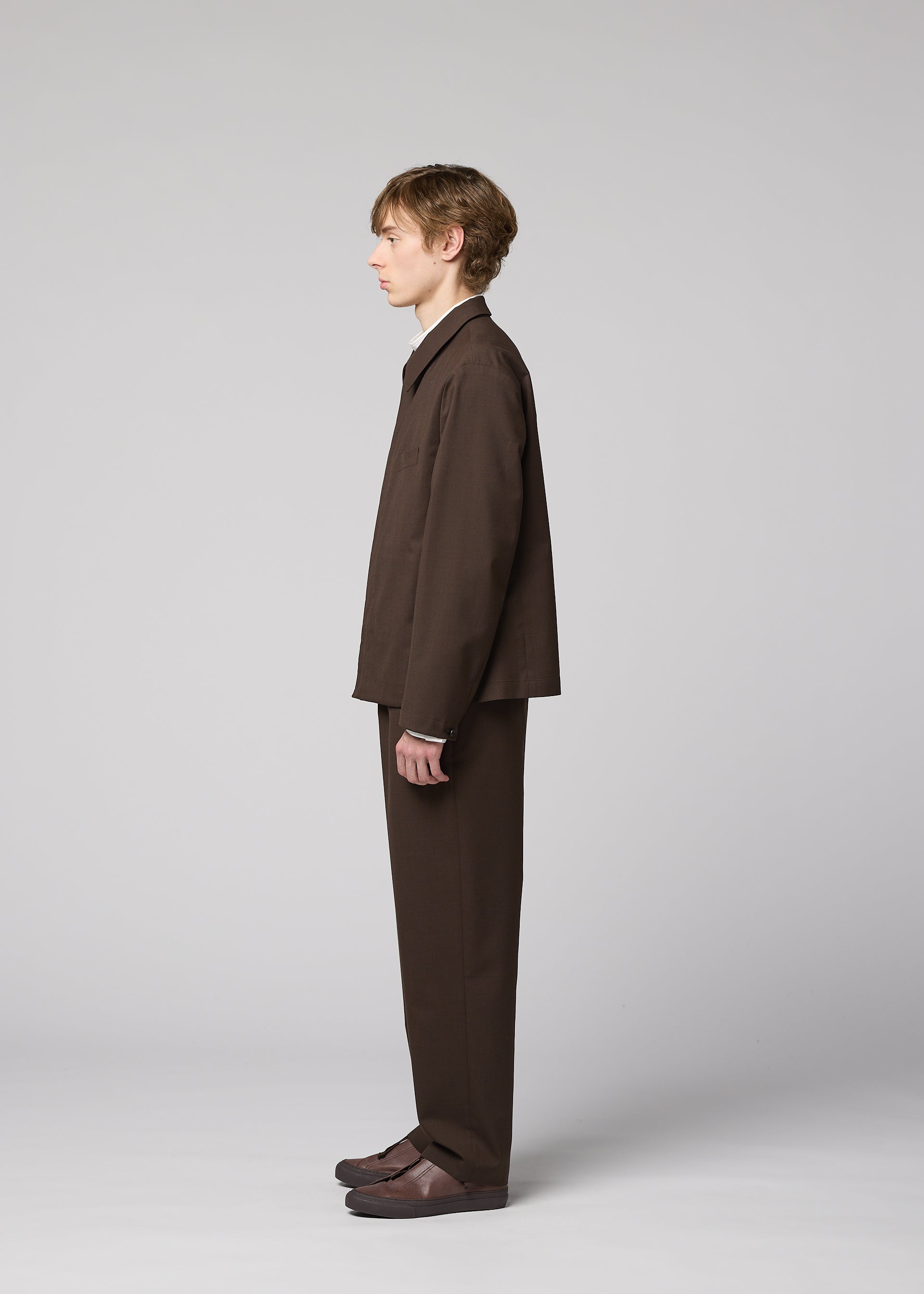 Zoomed view A person with short hair stands in profile against a plain background, wearing the IM MEN SUAVE loose-fitting wool blend jacket and matching pants, paired with brown shoes.