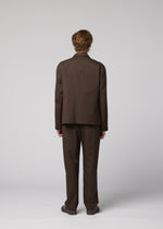 A person with short, light brown hair is seen from behind in a loose-fitting IM MEN SUAVE wool blend jacket and brown shoes, creating a sleek silhouette against a plain light gray background.