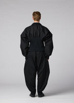 A person stands facing away against a plain, light gray background, wearing IM MEN’s CLAY set: a loose-fitting, all-black ensemble with wide sleeves and pants made from stretch fabric.