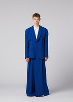 A person stands facing forward in an IM MEN SHRINK WOOL oversized royal blue jacket and wide-legged trousers over a white shirt, against a plain light grey background.