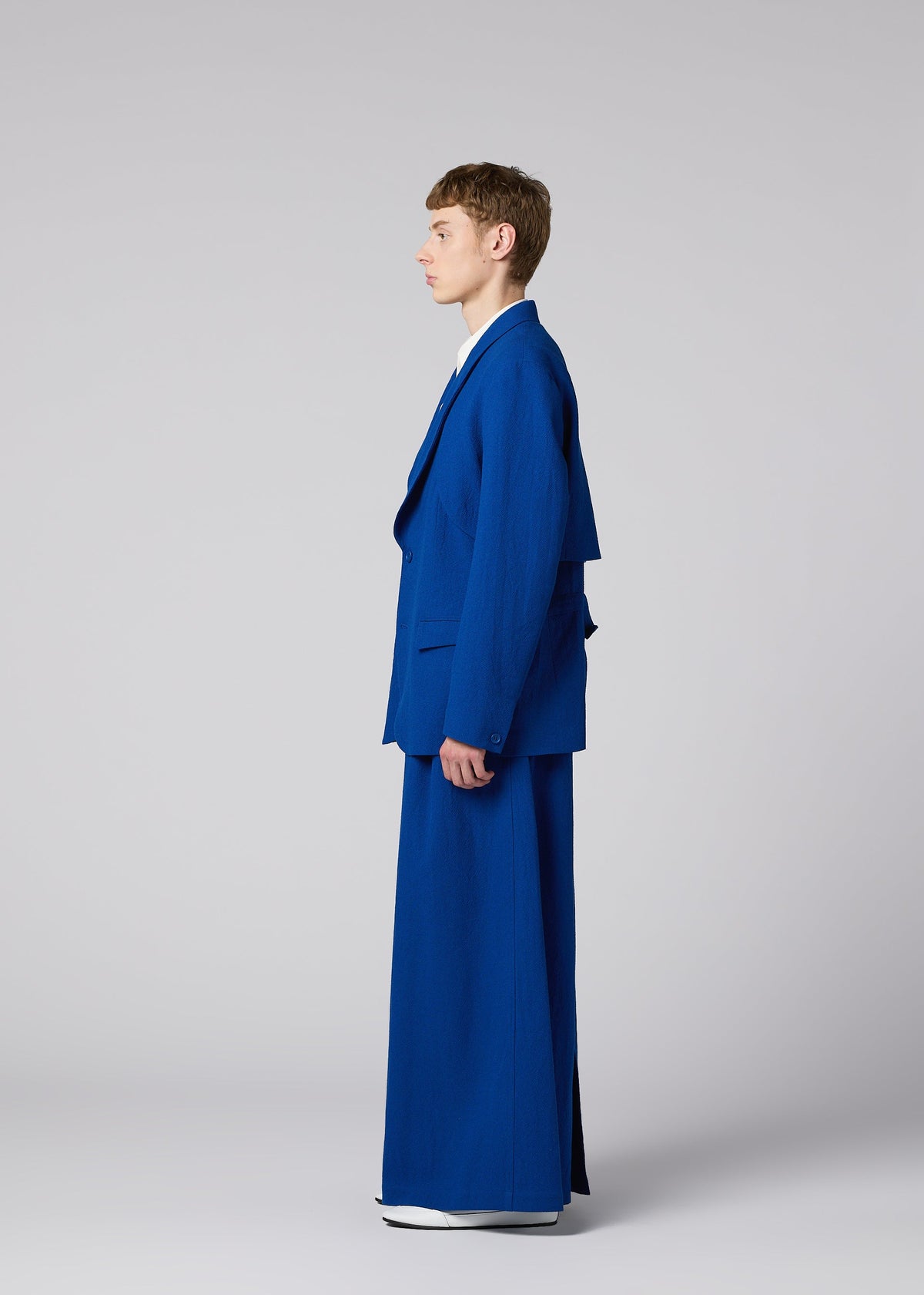 A person stands in profile wearing the SHRINK WOOL oversized jacket and extra-wide pants from IM MEN, Autumn Winter 2026/27 collection, against a plain light gray background. view 11 of 17