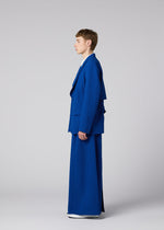 A person stands in profile wearing the SHRINK WOOL oversized jacket and extra-wide pants from IM MEN, Autumn Winter 2026/27 collection, against a plain light gray background.