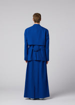 A person faces away, wearing a bright blue SHRINK WOOL jacket and matching floor-length skirt from IM MEN Autumn Winter 2026/27, set against a plain light background.