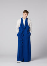 A person stands against a plain background wearing a white shirt and bright blue, oversized SHRINK WOOL jacket by IM MEN, with matching wide-leg pants and hands in pockets.