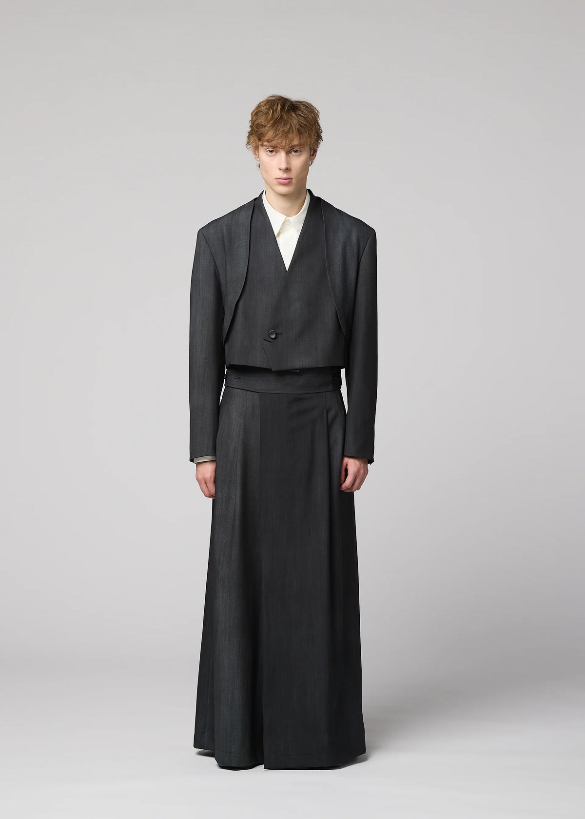 A person stands against a plain backdrop wearing an IM MEN GRADATION WOOL jacket and matching floor-length skirt, paired with a light-colored shirt. view 9 of 13