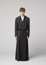 A person stands against a plain backdrop wearing an IM MEN GRADATION WOOL jacket and matching floor-length skirt, paired with a light-colored shirt.