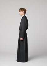 A person stands in profile against a plain background, wearing the IM MEN GRADATION WOOL tailored suit with a cropped jacket and wide, floor-length trousers from the Autumn Winter 2026/27 collection.