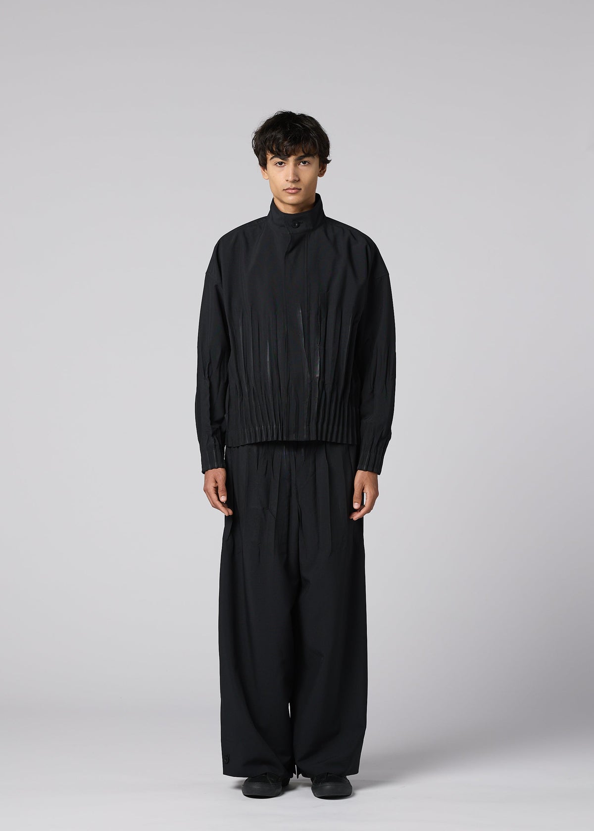 A person stands facing forward against a light gray background, wearing IM MEN's WAFT BLACK: a loose-fitting, linen-textured jacket with matching wide pants and black shoes. The adjustable hem and neutral expression complete the refined minimalist look. view 4 of 9