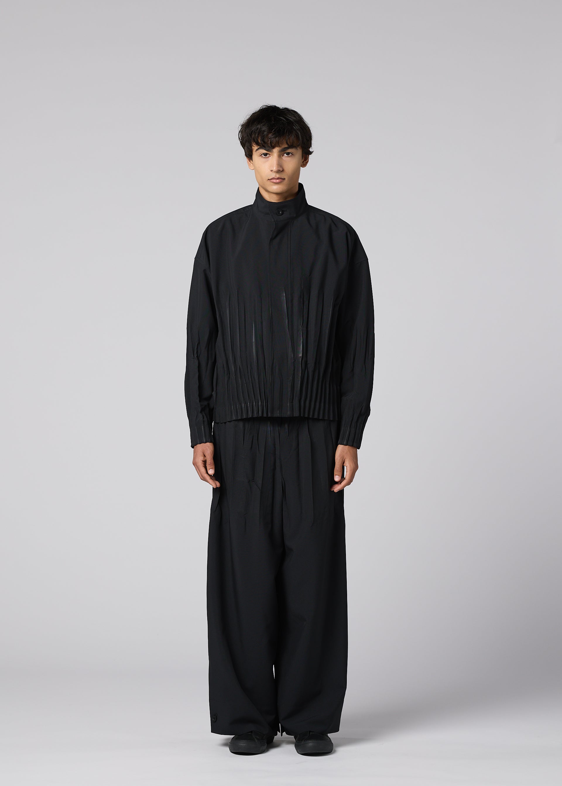 Zoomed view A person stands facing forward against a light gray background, wearing IM MEN's WAFT BLACK: a loose-fitting, linen-textured jacket with matching wide pants and black shoes. The adjustable hem and neutral expression complete the refined minimalist look.