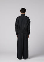 A person stands facing away, wearing IM MEN's WAFT BLACK— a loose-fitting black jacket with adjustable hem and gathered waist, paired with wide-leg, linen-textured black pants—set against a plain light gray background.