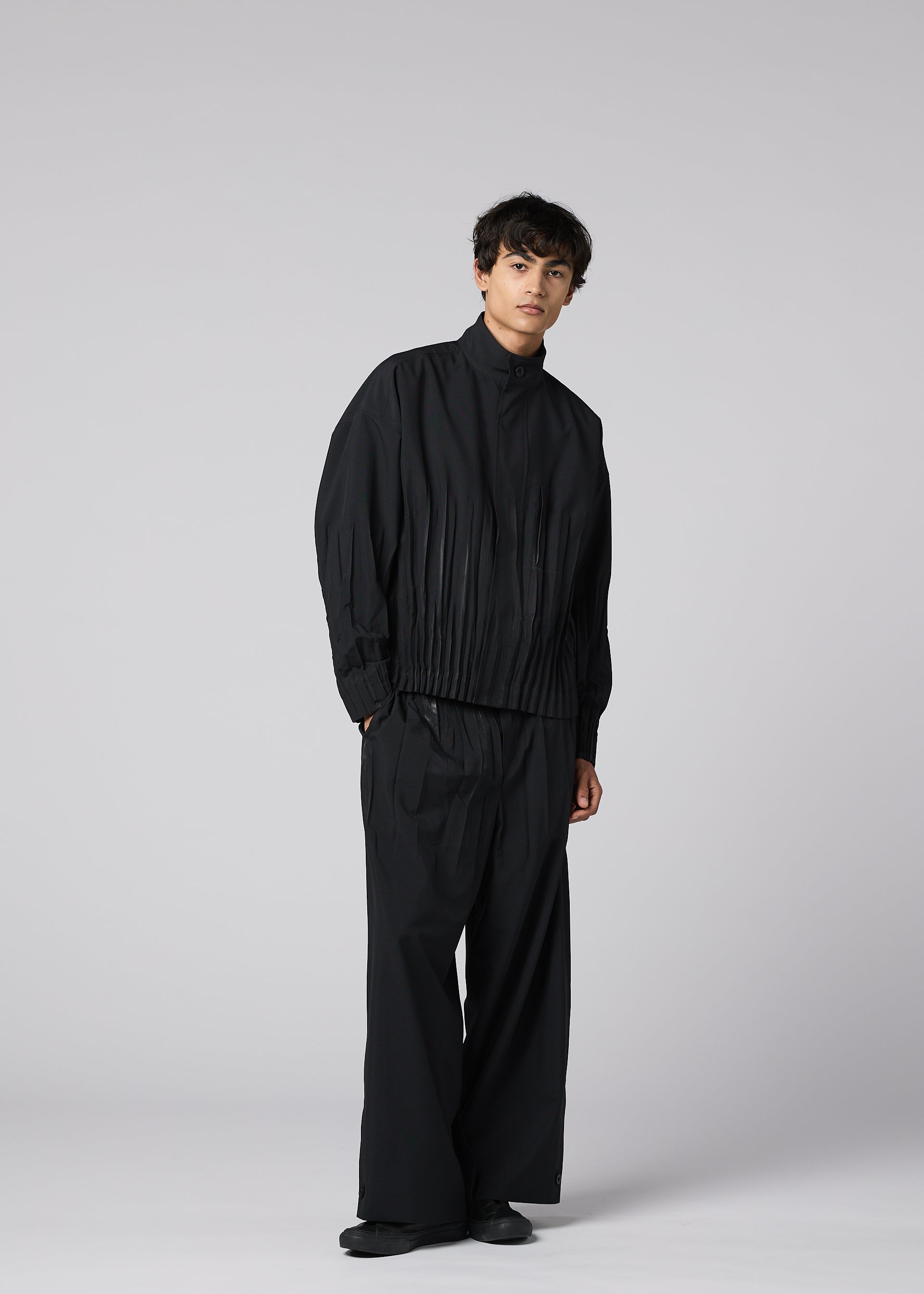 Zoomed view Against a plain light gray background, a person wears the WAFT BLACK jacket and wide adjustable-hem pants by IM MEN, featuring a linen-like texture. They are paired with black shoes, and the person gazes slightly to the side with a neutral expression.