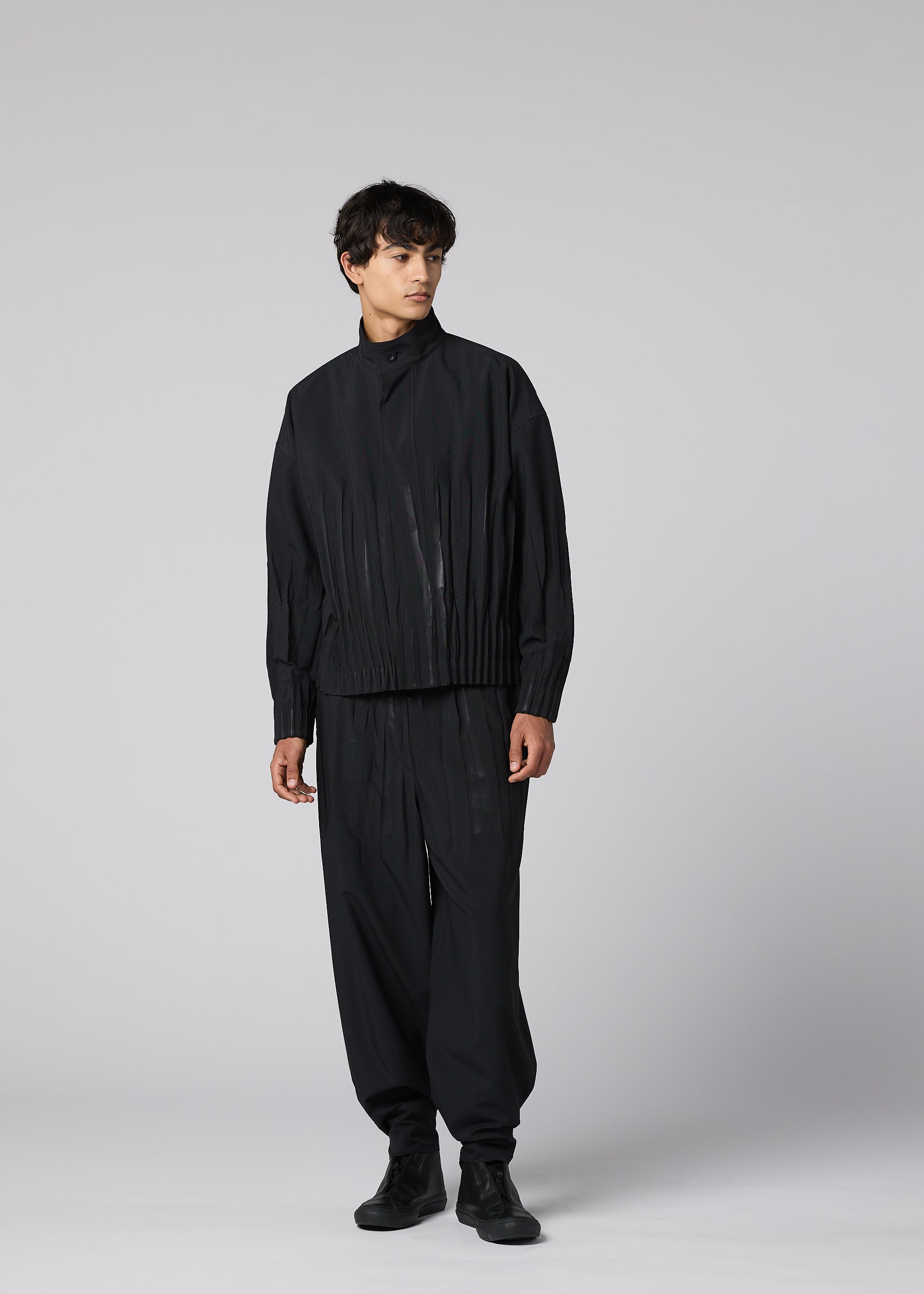 Zoomed view Against a plain gray background, a person wears IM MEN's WAFT BLACK: a relaxed-fit black jacket and wide, subtly striped pants with adjustable hem and linen-like texture, looking slightly sideways in a laid-back pose.