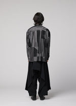 A person with medium-length dark hair stands facing away, wearing IM MEN’s COMFORT COTTON patterned gray and black jacket crafted from high-twist organic cotton, paired with loose irregular-cut black pants, against a plain light gray background.