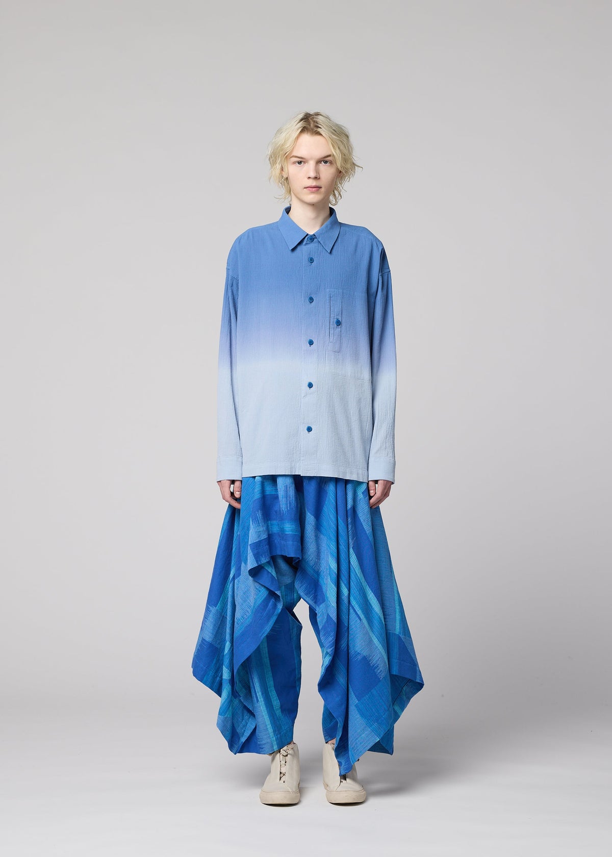 A person wearing the IM MEN KASURI loose gradient blue button-up shirt and wide, flowing pants—crafted with traditional Kasuri weaving—stands against a plain light gray background. view 5 of 8