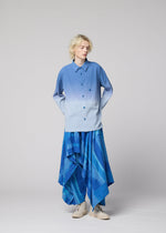 A person with blonde hair is wearing a loose, ombre blue IM MEN shirt and wide, flowy KASURI pants from IM MEN featuring subtle stripes, standing against a plain light gray background and looking slightly to the side.