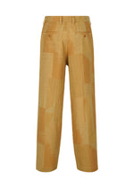 IM MEN’s KASURI pants feature a tan wide-leg silhouette with a geometric patchwork pattern in varying shades of brown, showcased from the back. Expertly crafted using traditional Kasuri weaving techniques, these pants are designed with belt loops, a back yoke, and two buttoned welt pockets.