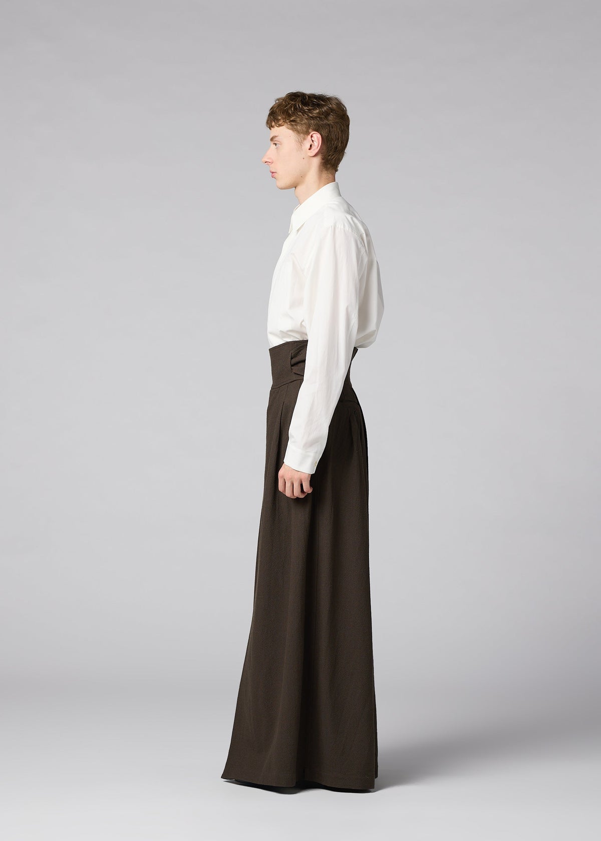 Zoomed view A person stands in profile against a gray background, wearing a white long-sleeve shirt tucked into IM MEN SHRINK WOOL high-waisted, wide pants.