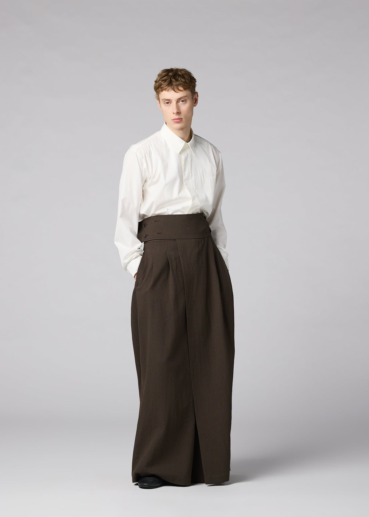 A person stands against a plain backdrop, wearing a white long-sleeve shirt and IM MEN’s SHRINK WOOL high-waisted, hard-twist wool wide pants for a minimal, modern look. view 8 of 8