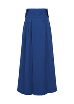 The IM MEN SHRINK WOOL is a long, high-waisted royal blue skirt in hard-twist wool, featuring a wide waistband, front pleats, two hip buttons, and a structured, slightly flared silhouette for elegant style.