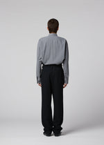 A person faces away from the camera, wearing a gray long-sleeve shirt and black SHRINK WOOL pants by IM MEN, against a plain light gray background.