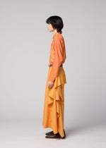 A person stands in profile against a plain background, wearing the IM MEN BREEZE DRAPE flowy pants and a matching orange long-sleeve shirt, paired with brown shoes.