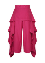 IM MEN’s BREEZE DRAPE pants feature a vibrant pink hue and a high-waisted fit, with layered cascading fabric panels along each side that create a skirt-like effect over the shorts—offering a chic, modern take on classic flowy pants.