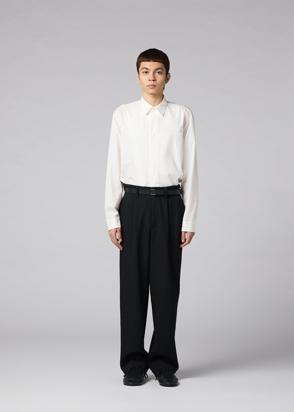 A person stands facing forward, wearing IM MEN’s FRONT BACK white button-up shirt tucked into loose matte wool trousers with a belt, paired with black shoes, against a plain light gray background. view 4 of 7