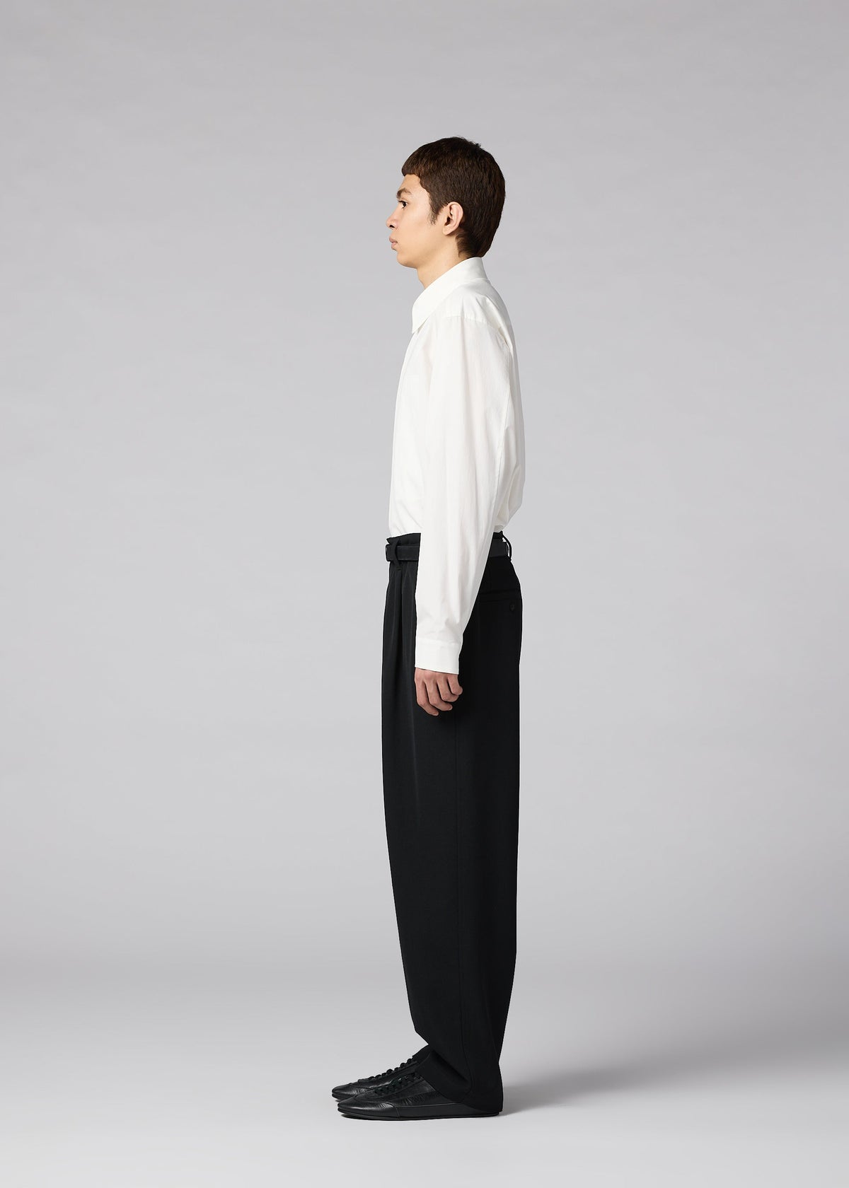 A person stands in profile against a plain gray background, wearing a white dress shirt, IM MEN’s FRONT BACK men’s autumn winter pants in classic black, and coordinating black shoes. view 5 of 7