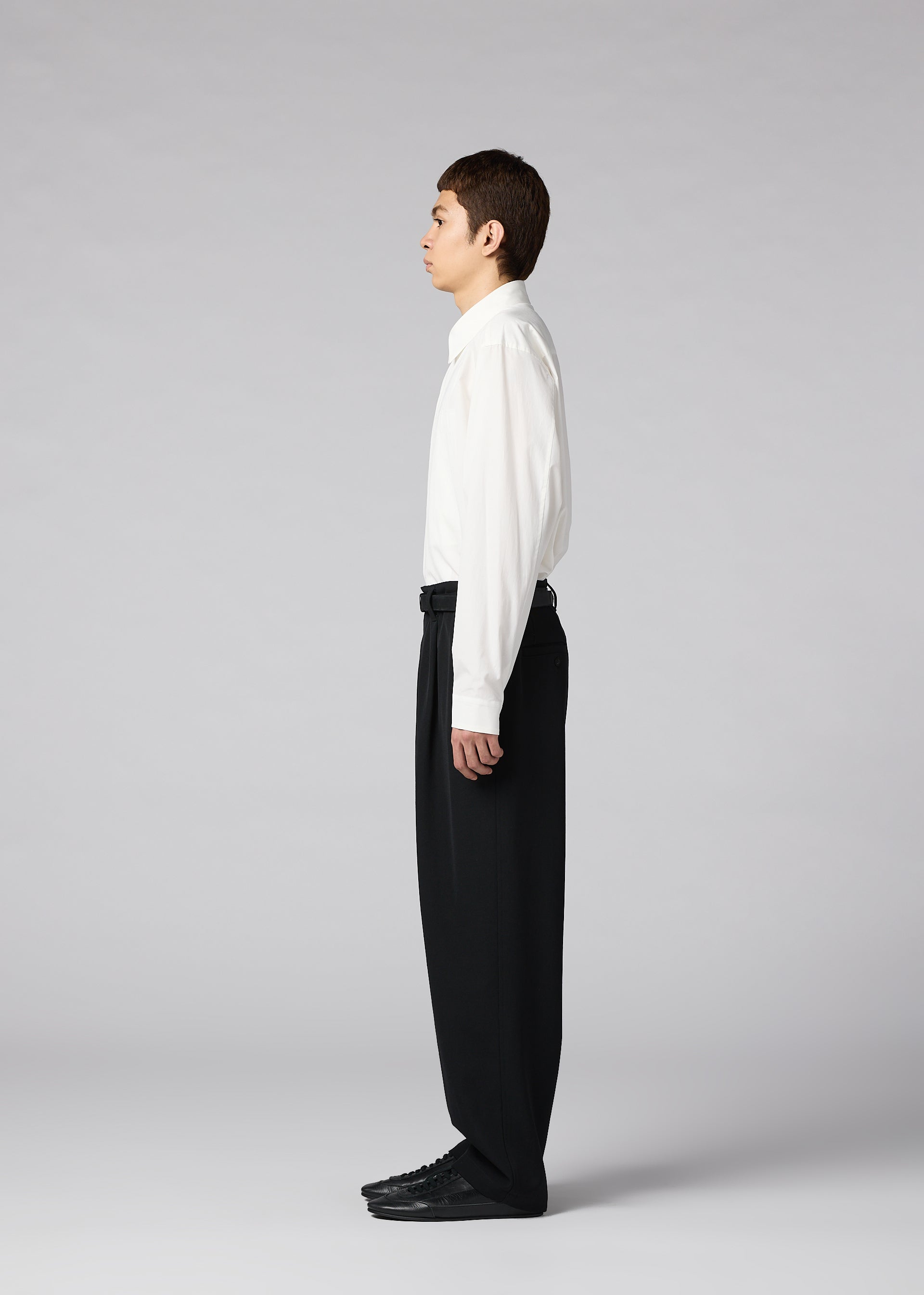 Zoomed view A person stands in profile against a plain gray background, wearing a white dress shirt, IM MEN’s FRONT BACK men’s autumn winter pants in classic black, and coordinating black shoes.